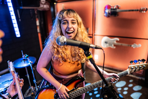 Young woman singing and playing electric bass on a show