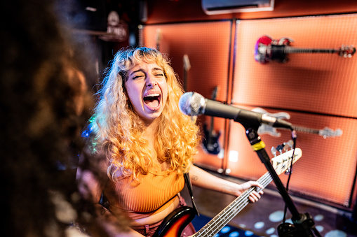 Young woman singing and playing electric bass on a show
