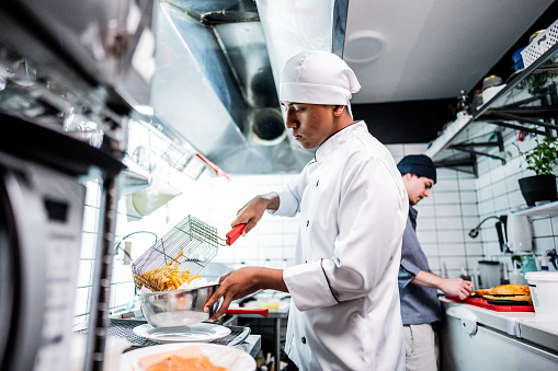 Chef young man making fries on a commercial kitchen