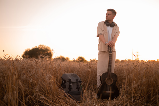 A man with a guitar in the camp. Songs by the fire. Acoustic guitarist in the countryside, musical song. Sexy man with a guitar in a shirt. Hipster fashion