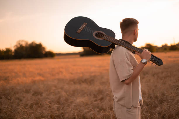 un homme avec une guitare dans le camp. chansons au coin du feu. guitariste acoustique à la campagne, chanson musicale. homme sexy avec une guitare en chemise. mode hipster - musical instrument nature outdoors musician photos et images de collection