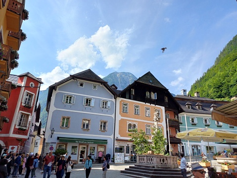 Hallstatt, Austria - June 7, 2023: Scenic view of houses in center square of Hallstatt mountain town with blue sky clouds in background.