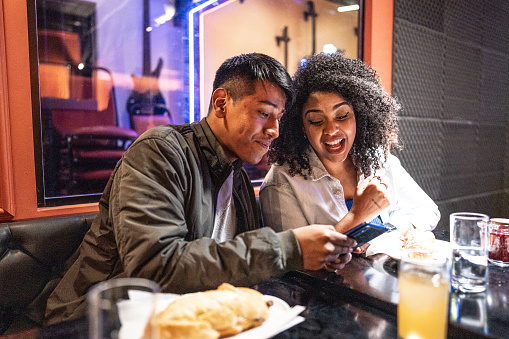 Young man showing mobile phone to his friend on a restaurant