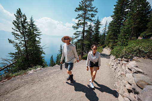 An active and healthy retired man hikes with his Eurasian adult daughter up a mountain trail near Crater Lake in Oregon during a fun and adventurous multi-generation camping vacation.