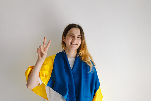 Cheerful ukrainian girl that shows a sign of peace or victory. Portrait of a teenage girl with the Ukrainian flag on a white background. Lifestyle