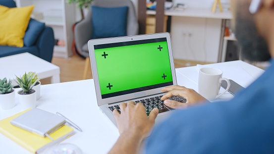 African American man looking at pre-keyed laptop green screen, typing on keyboard