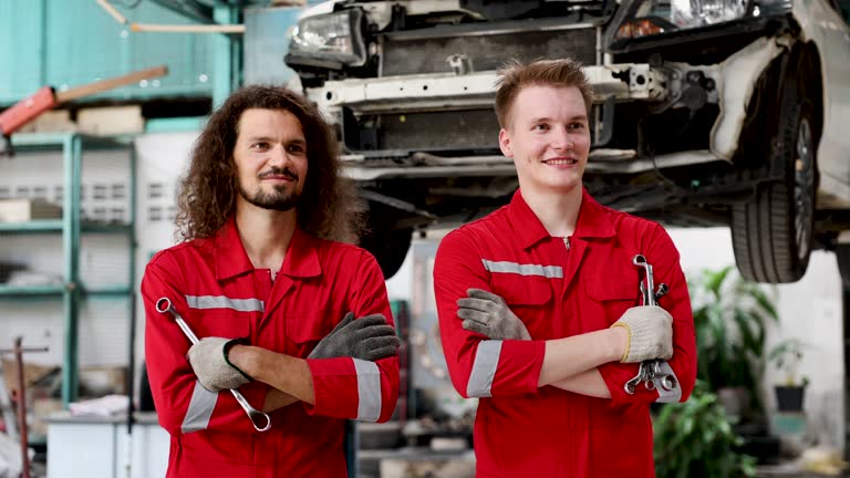 Two attractive Caucasian mechanics cross arm looking at camera holding wrenches smiling in front of garage, Young technicians' friends or entrepreneur partners design to open car repair services