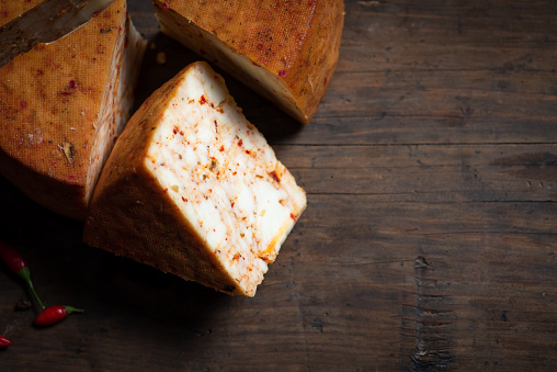 Homemade hard cow's cheese with red pepper on a wooden table