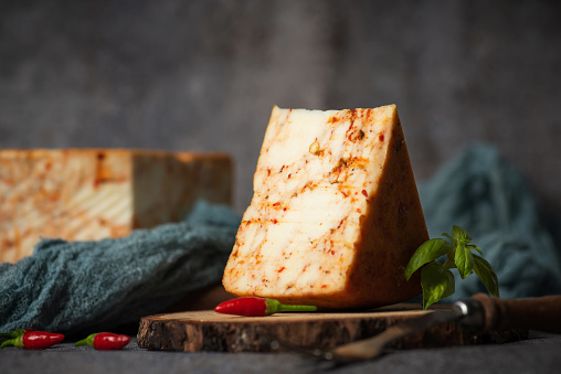 Homemade hard cow's cheese with red pepper on a wooden board and rustic gray background