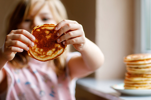 Little happy preschool girl with a large stack of pancakes for breakfast. Positive child eating healthy homemade food in the morning