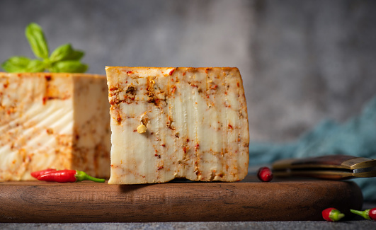 Homemade hard cow's cheese with red pepper on a wooden board and rustic gray background