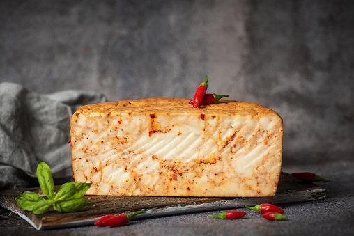 Homemade hard cow's cheese with red pepper on a wooden board and rustic gray background