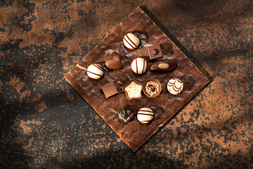 Handmade delicious chocolate candies of different shapes, from white and dark chocolate, on a rustic brown background