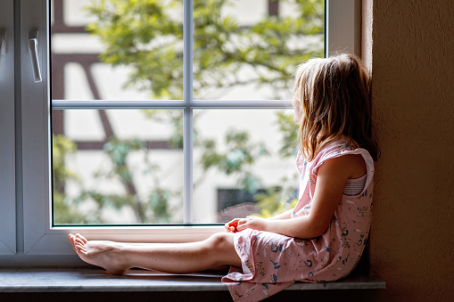 Adorable little girl sitting by the window. preschool child looking out and dreaming