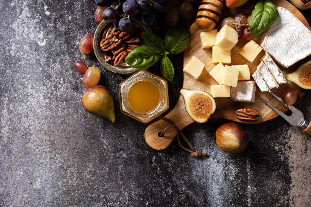 istock Brie cheese, fresh figs, grapes, cheese cubes, pears, pecan nuts and honey on cutting board on dark stone background. Cheese plate, still life of seasonal wine snacks. View from above. Copy space. 1668226518