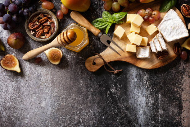 istock Brie cheese, fresh figs, grapes, cheese cubes, pears, pecan nuts and honey on cutting board on dark stone background. Cheese plate, still life of seasonal wine snacks. View from above. Copy space. 1668226522
