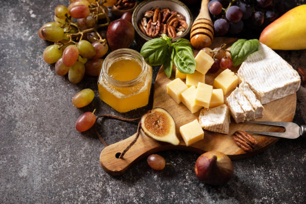 istock Brie cheese, fresh figs, grapes, cheese cubes, pears, pecan nuts and honey on cutting board on dark stone background. Cheese plate, still life of seasonal wine snacks. 1668226526