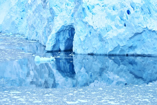 A colorful glacier and ice cave are reflected in the ice filled waters of the Antarctic Peninsula.