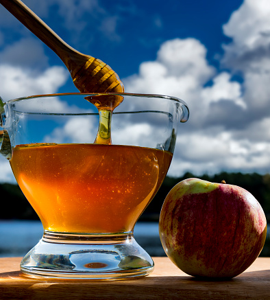 Close up with jar or jug of honey and apple - main symbols of Jewish New Year and sweet holiday - Rosh Hashanah. Natural background with blurred river, forest and clouds
