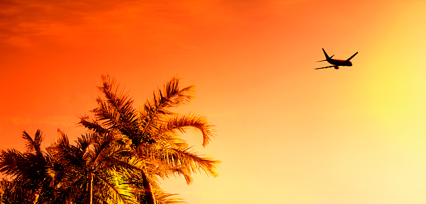 Transportation image of flying commercial passenger airplane over orange color sunset sky in Florida