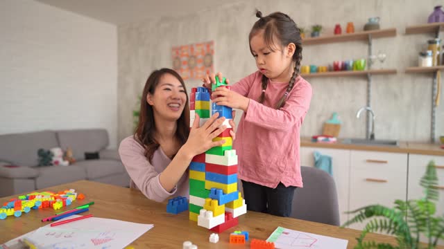 Mother And Her Daughter Playing With Building Blocks On The Dining Table