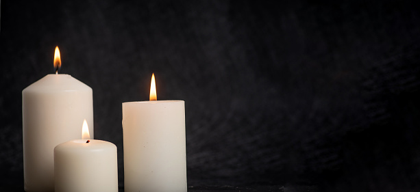 Three burning white, decorative, scented candles of different sizes on a black background