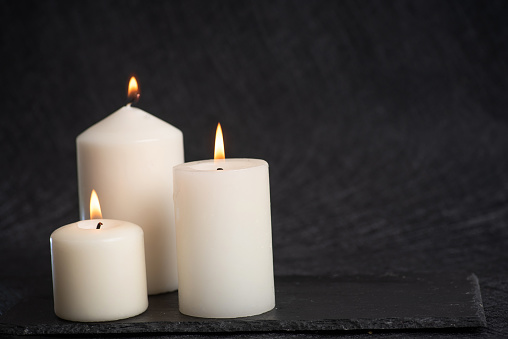 Three burning white, decorative, scented candles of different sizes on a black background