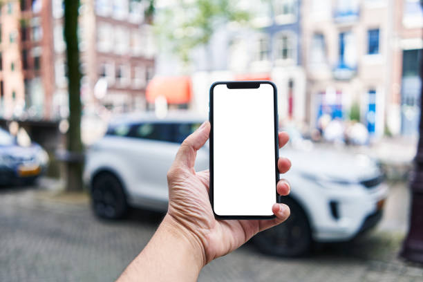 istock Man holding smartphone showing white blank screen at car parking 1668351577