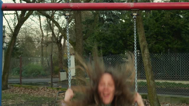 Teenager girl with long curly hair has fun riding swing outdoors on autumn day.