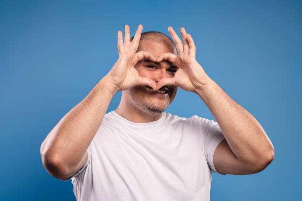 portrait of a brazilian man wearing a basic white shirt, from the front, making a heart with his hands, raised at eye level, looking at the camera and smiling - belém - pará - brazil - human heart flash imagens e fotografias de stock