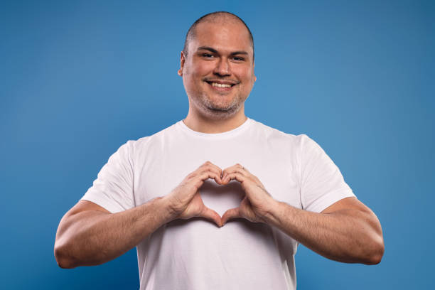 ritratto di un uomo brasiliano che indossa una camicia bianca di base, dal davanti, facendo un cuore con le mani, sollevate all'altezza del petto, guardando la macchina fotografica e sorridendo - belém - pará - brasile - human heart flash foto e immagini stock