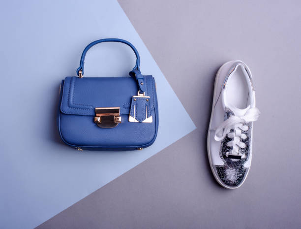 Stylish female blue leather top-handle bag and white-silver sneaker with a cracked effect on a two-tone background. Top view, flat lay. Fashion blog. Creating a fashionable outfit by a stylist.
