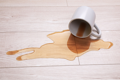 White mug with spilled liquid on wooden floor