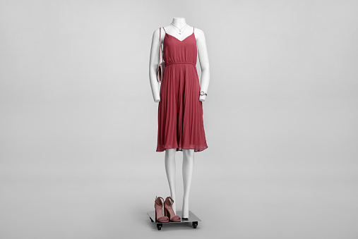 Female mannequin with necklace and bag dressed in stylish red dress on grey background
