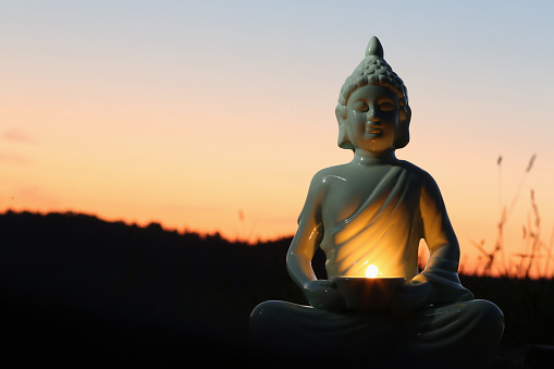 istock Decorative Buddha statue with burning candle outdoors at sunset. Space for text 1668553193