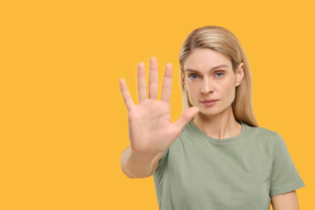 istock Woman showing stop gesture on yellow background. Space for text 1668577578