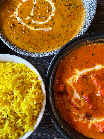 Stock photo showing close-up, elevated view of Chicken Tikka Masala, Dal makhani curry and pilau rice in serving bowls as part of Indian meal in a restaurant.