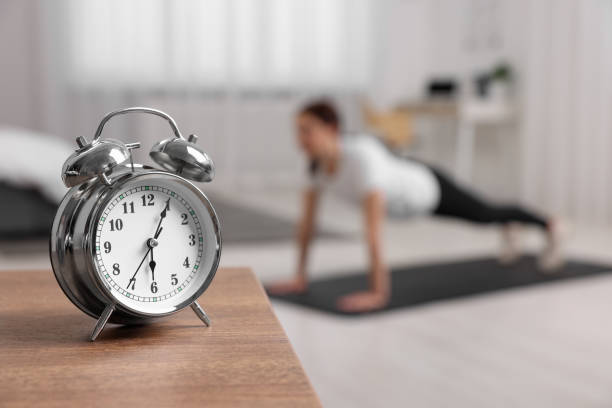 istock Morning routine. Alarm clock on wooden table and woman doing exercise, selective focus. Space for text 1668594543