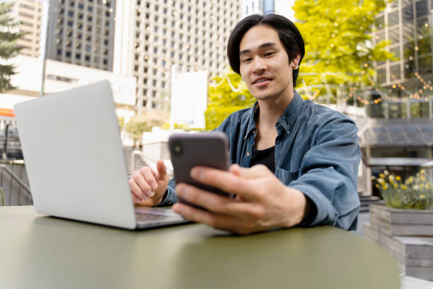istock Handsome confident japanese businessman using laptop, holding mobile phone, working outdoors in cafe 1668666877