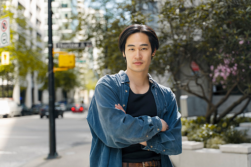 Portrait of handsome confident Japanese man holding arms crossed wearing stylish casual outfit looking at camera standing on the street. Beauty concept
