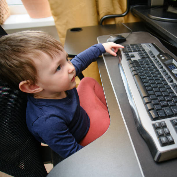 istock Toddler baby works on a computer with a keyboard and mouse. Happy child sits on a computer chair next to the PC. Kid age one year nine months 1668724331