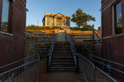 Stairs lead to the Osage County Courthouse in Pawhuska, Oklahoma, which is in morning sunlight, on a hill above the business district of the small town.  The courthouse was the site of the trials relating to Osage murders in the early 20th century, depicted in the Killers of the Flower Moon book and movie.