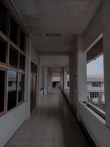 This photo captures a long hallway with windows and a balcony in a building. The hallway is made of concrete and it has a white ceiling. The windows are large and they let in a lot of natural light. The balcony is located at the end of the hallway and it offers a view of the city. The image is both elegant and modern, and it could be used to represent a variety of concepts, such as architecture, design, and interior.
