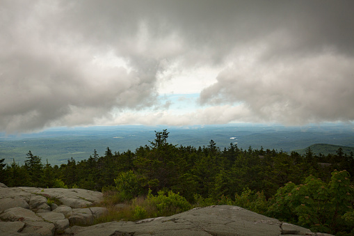 Passing dark rain cloud floating by, seen from the exposed bedrock summit of Mt. Kearsarge, at Winslow State Park in Wilmot, New Hampshire