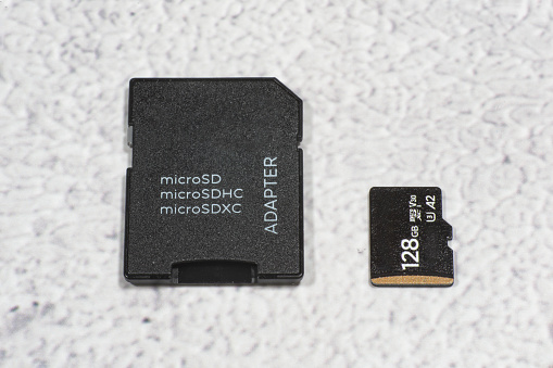 Top view of a microSD memory card with SD adapter against mottled gray background.