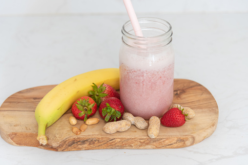 Strawberry banana peanut butter super food smoothie in jar on cutting board with ingredients