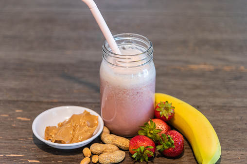 Strawberry banana peanut butter smoothie in glass with ingredients on wood table