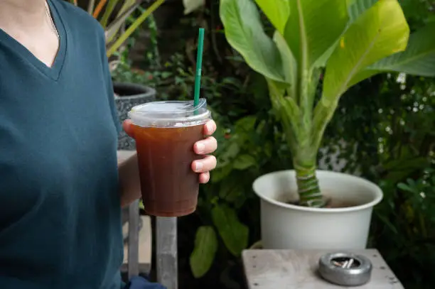 Photo of Cropped shot view of woman hand holding a plastic cup of iced americano coffee.