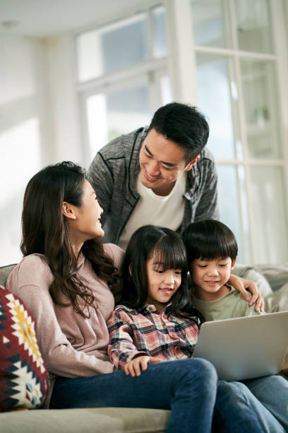young asian couple and two children using laptop computer together at home stock photo