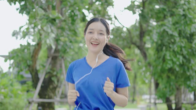Young asian woman runner wearing headphones to listen to music while running in park. Close up fitness girl jogging outdoor. Morning running concept, healthy way of life, staying fit concept, 4k